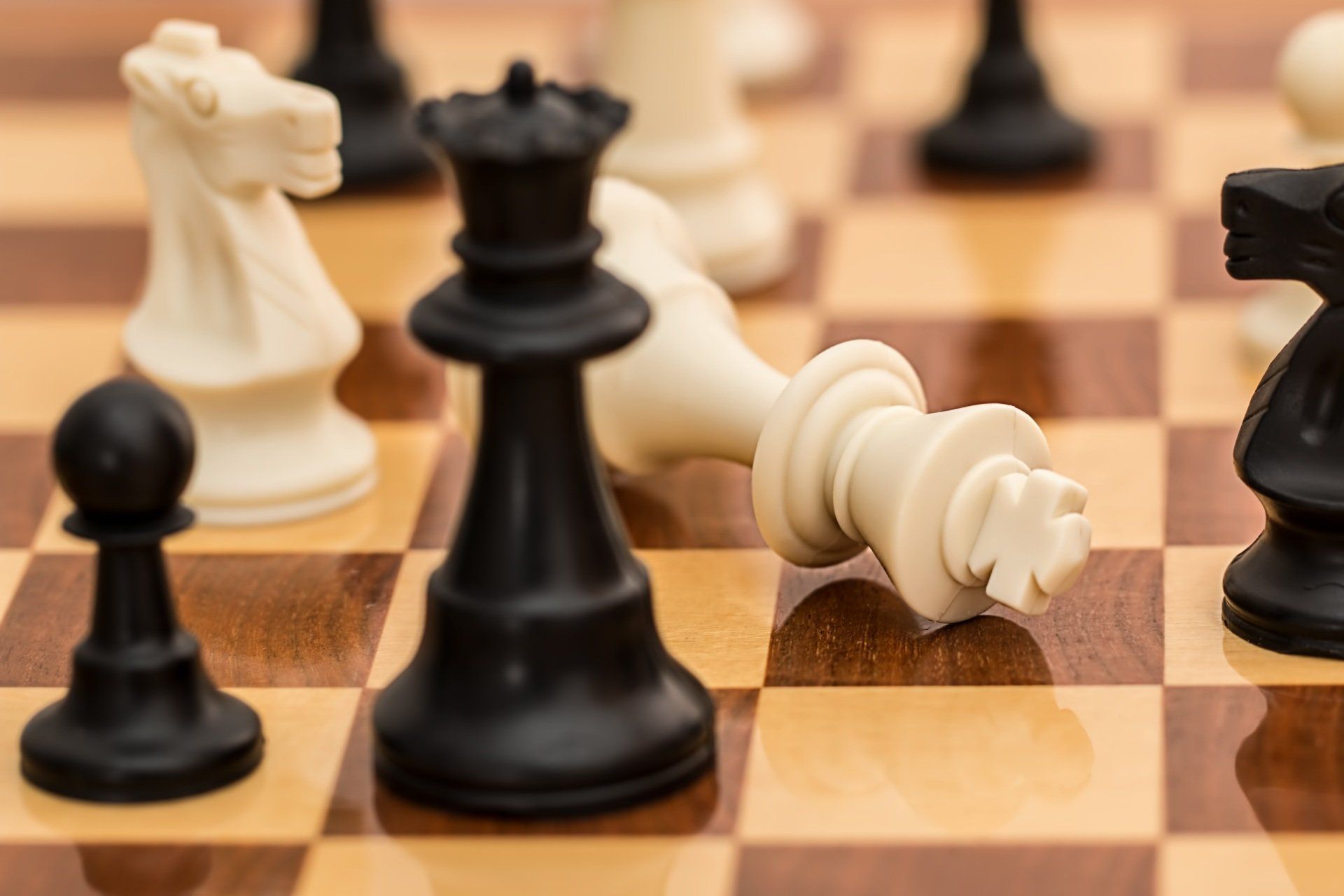 Chessboard with fallen white king; black queen, knight, and pawn surround it.