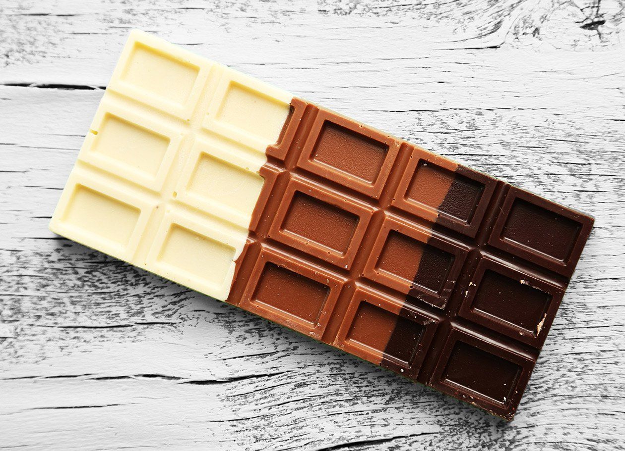 Chocolate bar, white, milk, and dark chocolate sections on white wood.