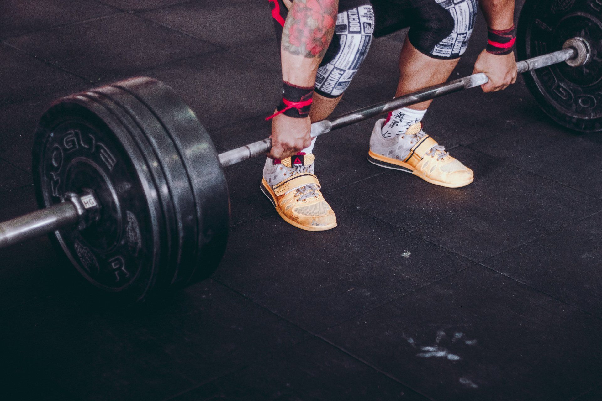 Weightlifter gripping barbell on black gym floor, knees bent, lifting weights.