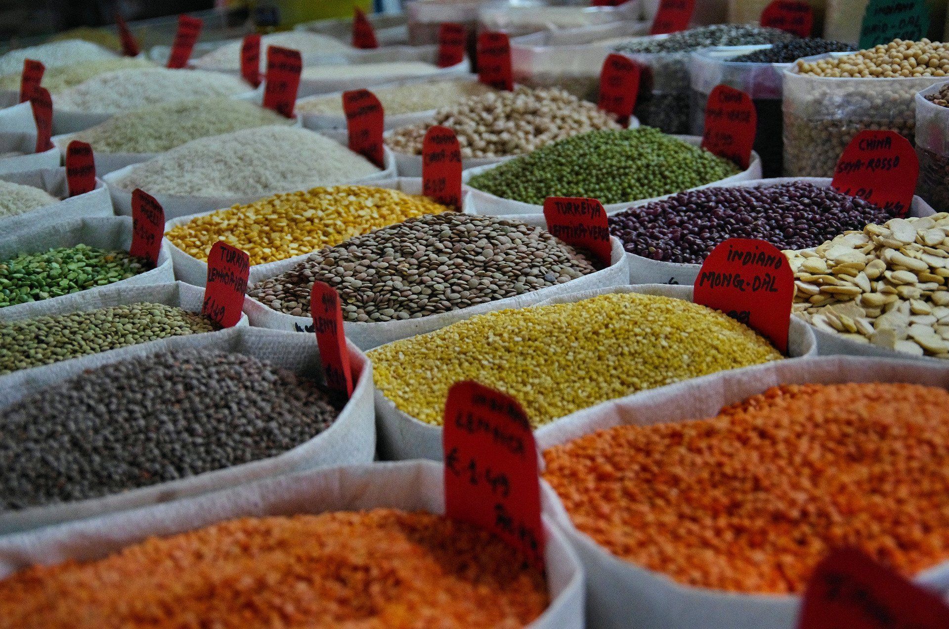Bags filled with a variety of grains and legumes, including lentils, beans, and rice. Red price tags are visible.