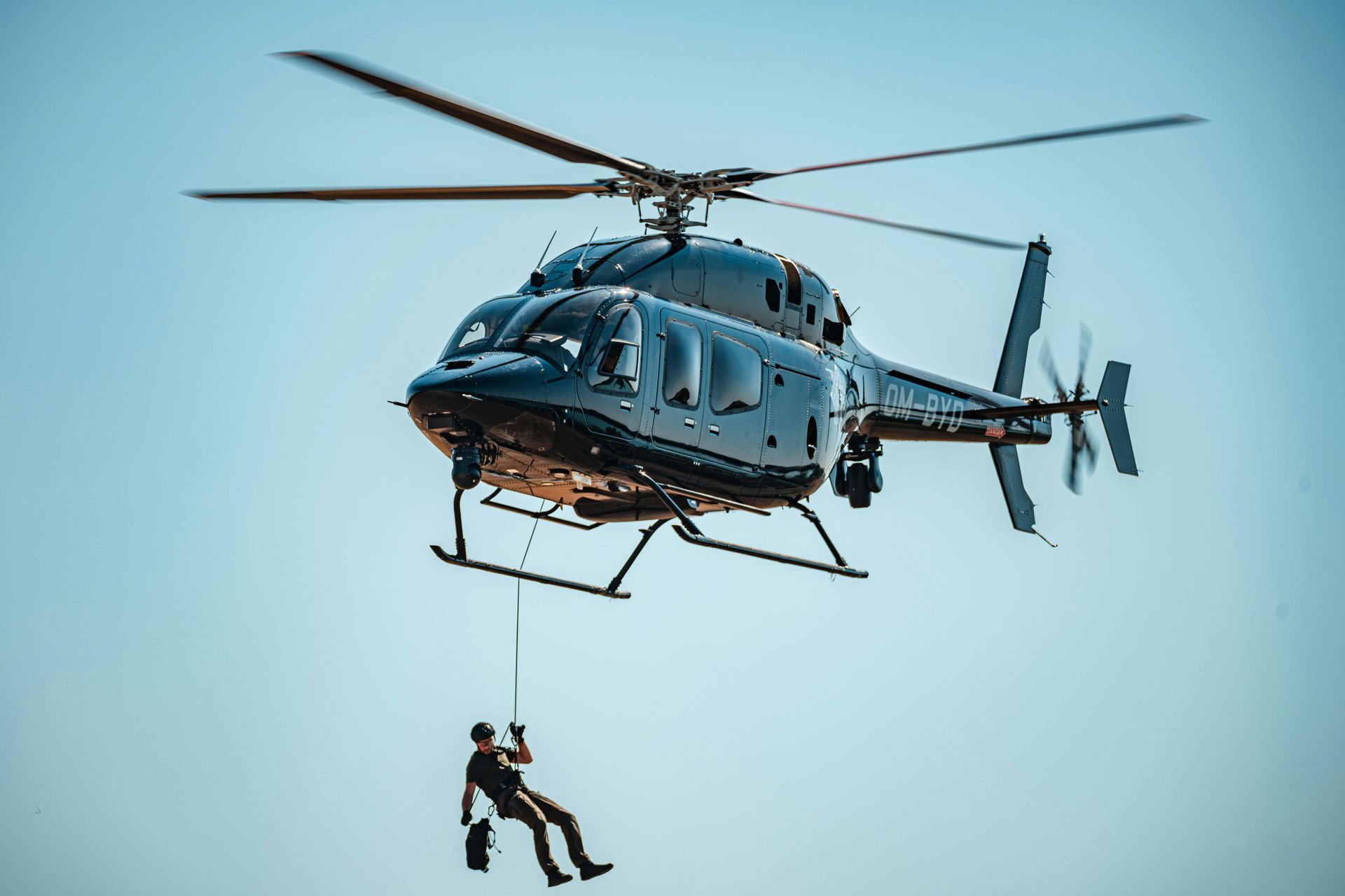 Helicopter with person rappelling down against a blue sky.