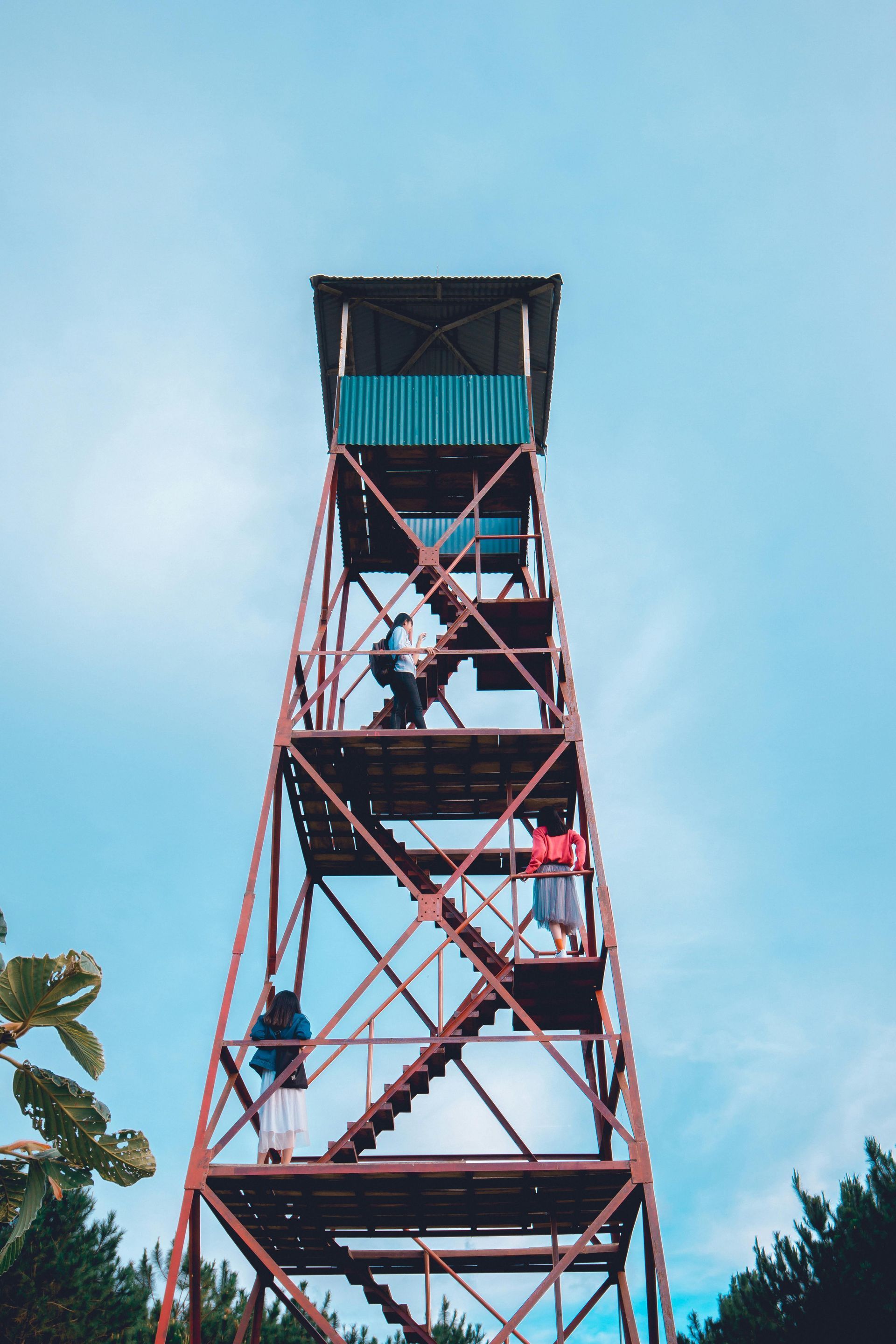 Rusty fire tower, people climbing stairs, blue sky backdrop.
