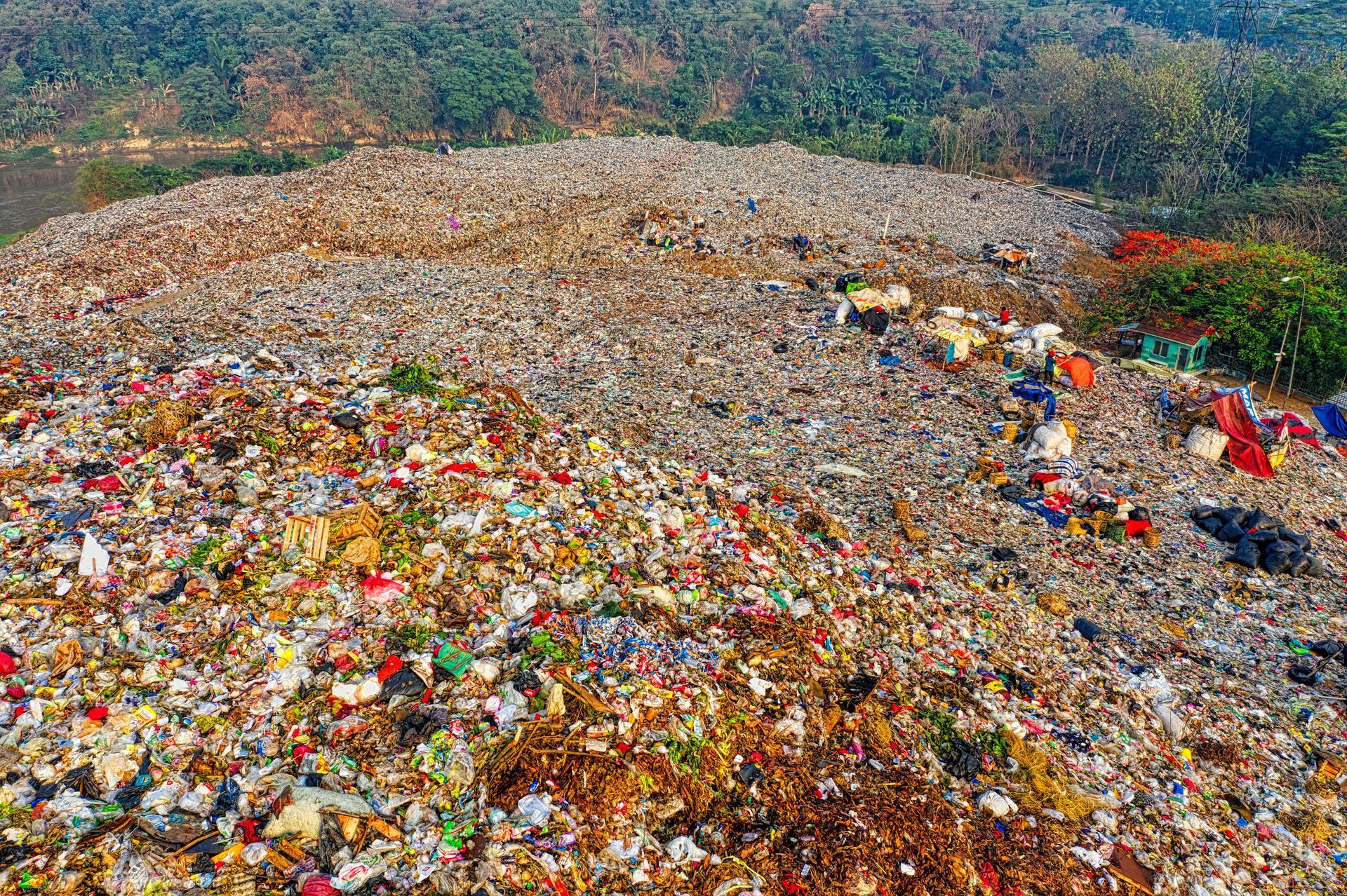 Large pile of trash and waste, outdoors near trees. Various colors of debris cover the hillside.