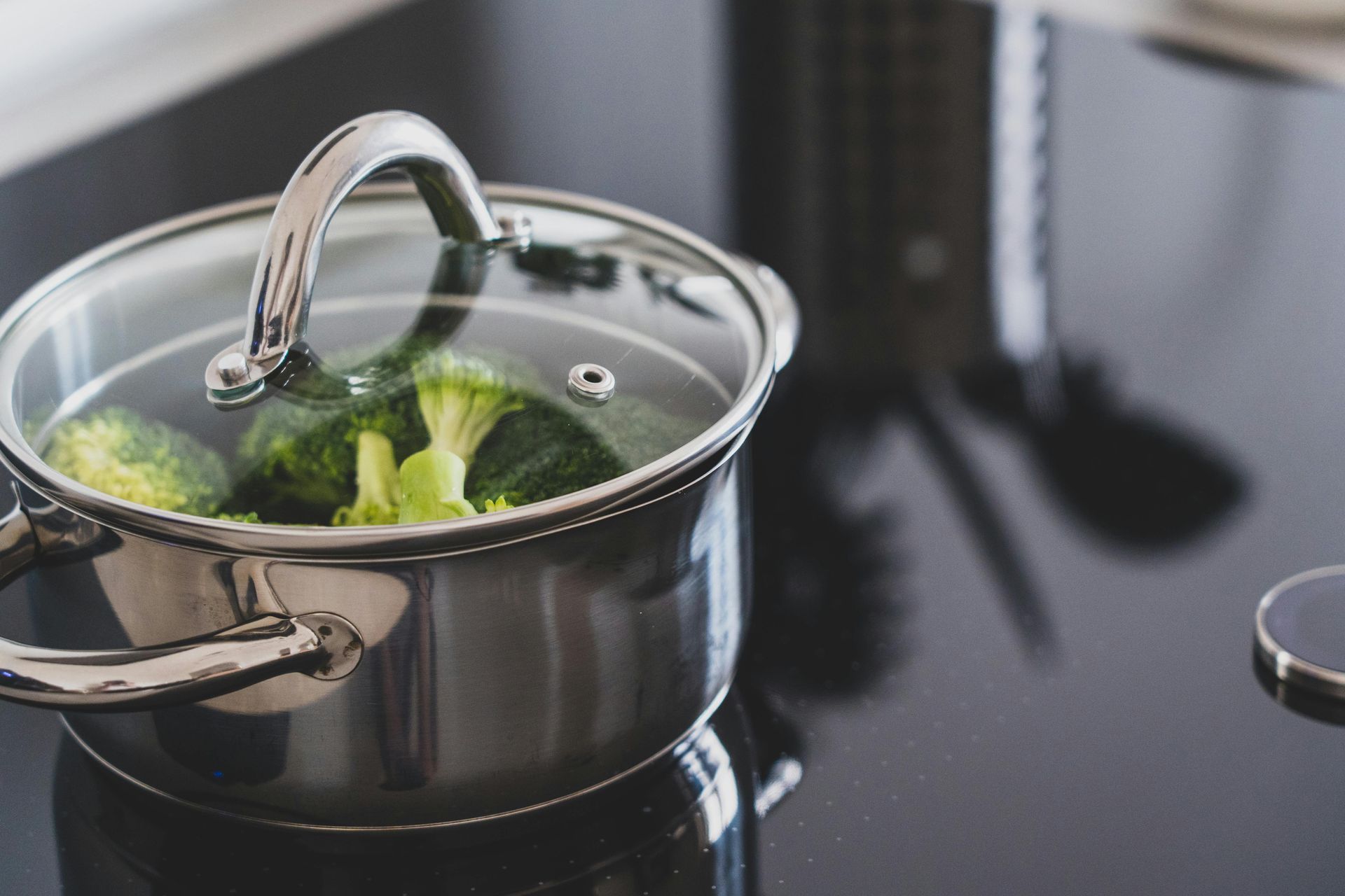 Pot of broccoli steaming on a black stovetop, covered with a glass lid.