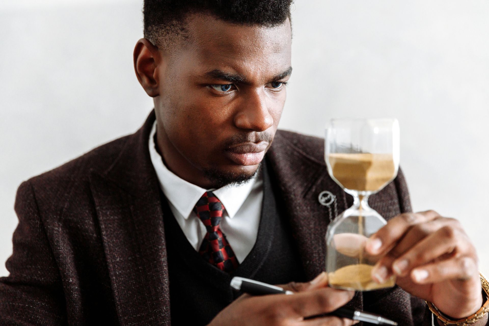Man in suit intently watches sand flow through hourglass.
