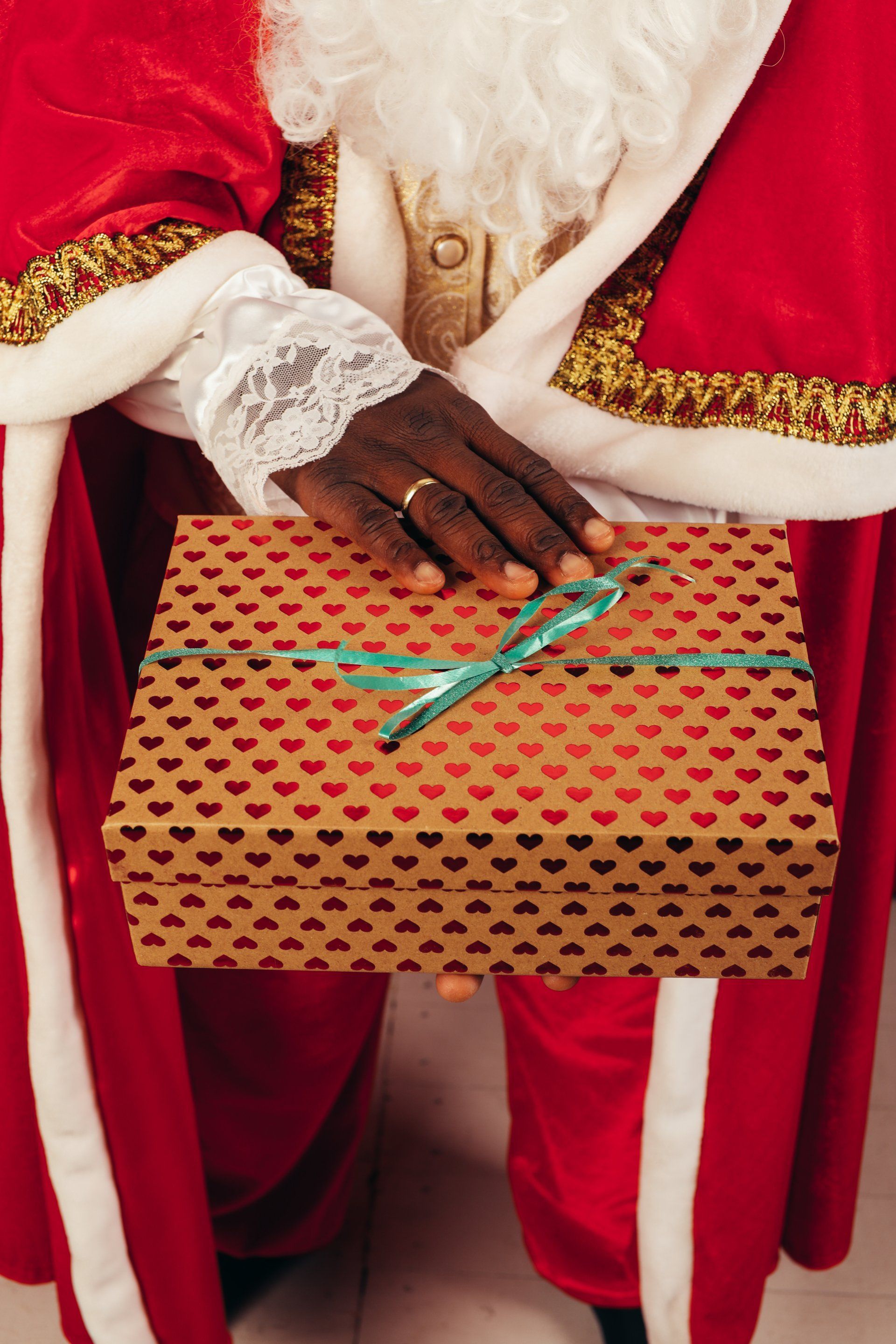 Santa Claus holding a present wrapped in brown paper with red hearts and a turquoise bow.