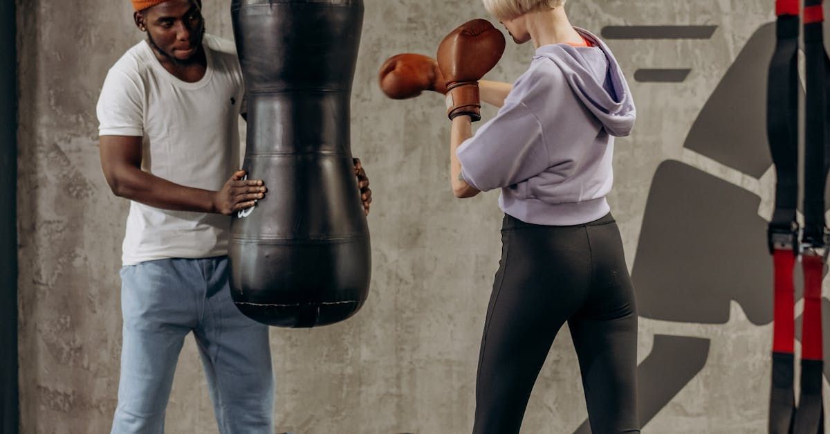 Person boxing with gloves, assisted by another holding the punching bag in a gym.