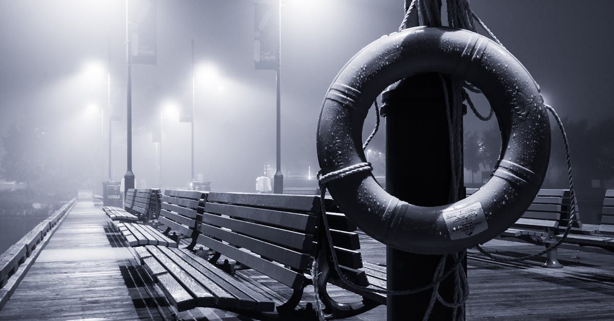 Pier at night, foggy, with benches, streetlights, and life preserver.