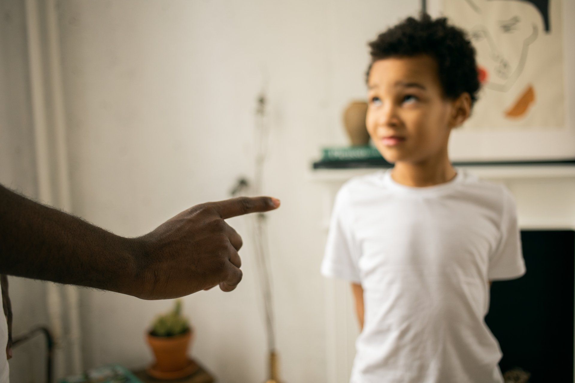 Finger pointing at a young child, who is looking up with a worried expression, indoors.