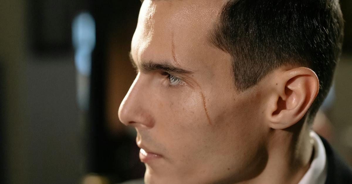 Man with a scar on his cheek, looking to the side. Wearing a dark suit, indoors.