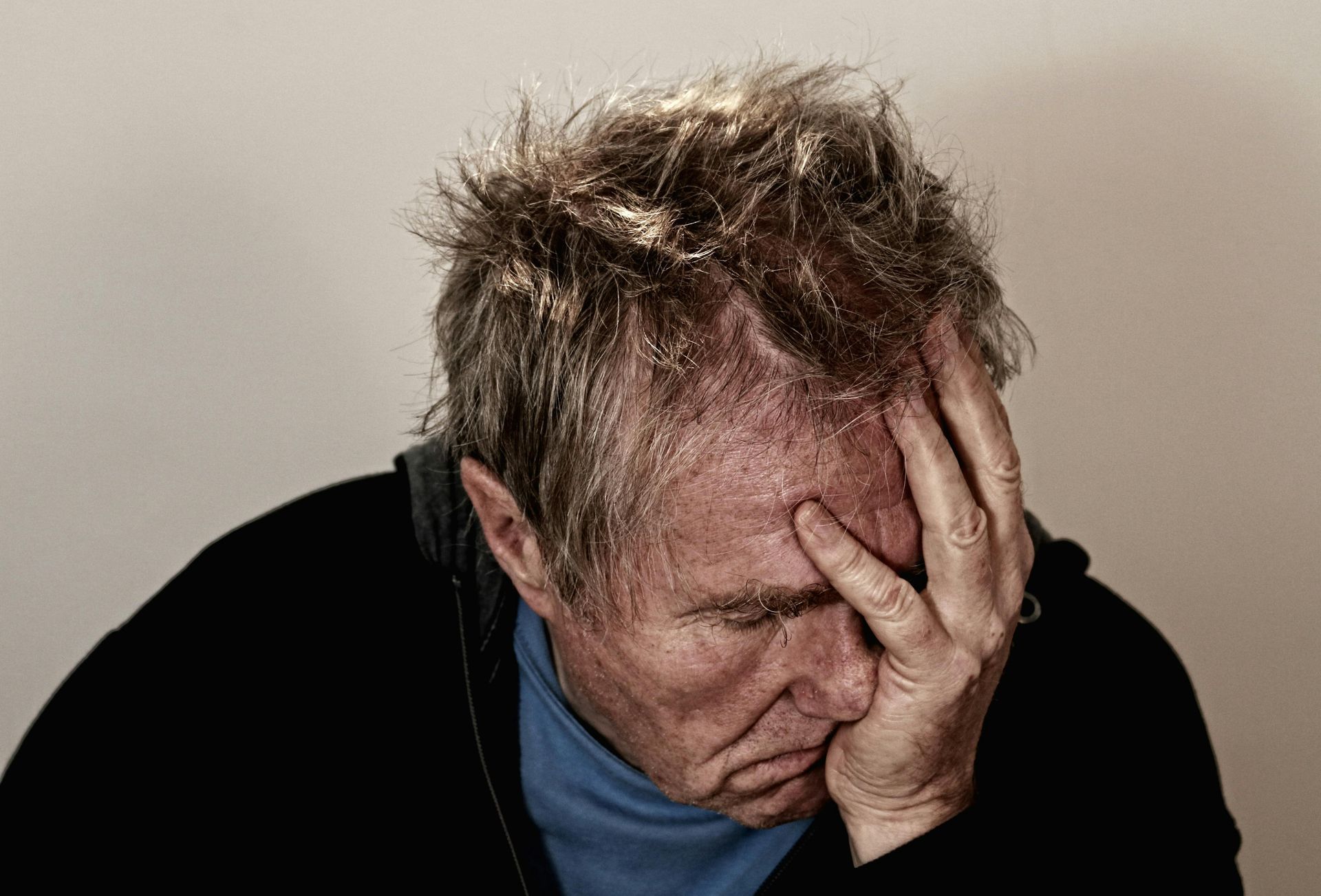 Man with hand on forehead, looking down, showing sadness, likely overwhelmed or in distress.