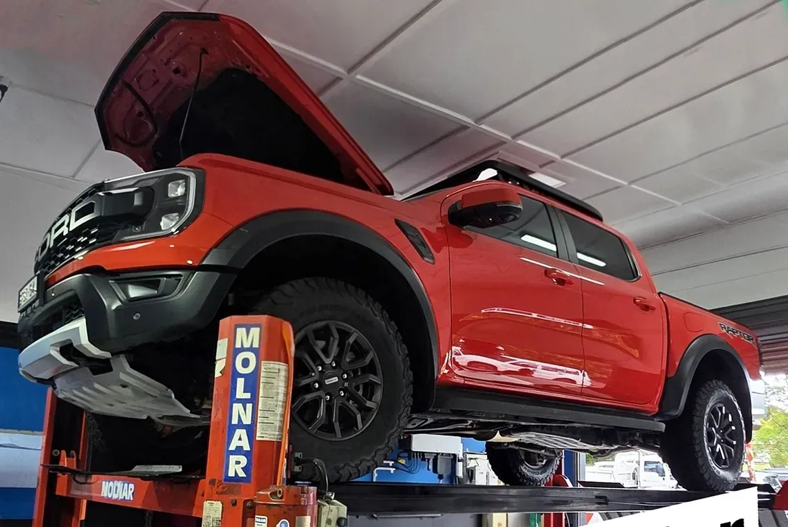 A Red Truck on a Hoist in a Garage — M T Automotive In Wallsend, NSW