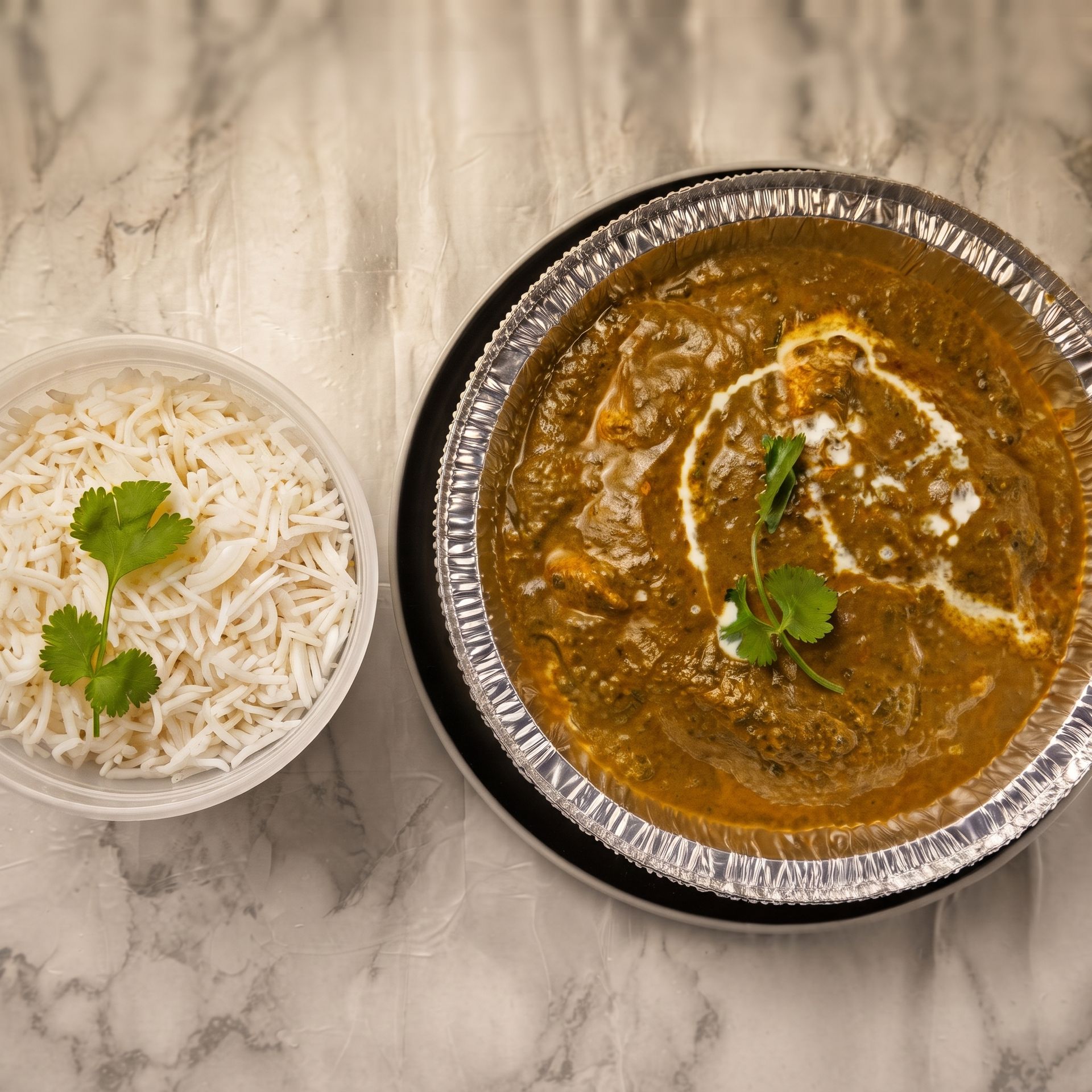 Takeout curry and rice in bowls on a marble table, garnished with cilantro and cream drizzle.