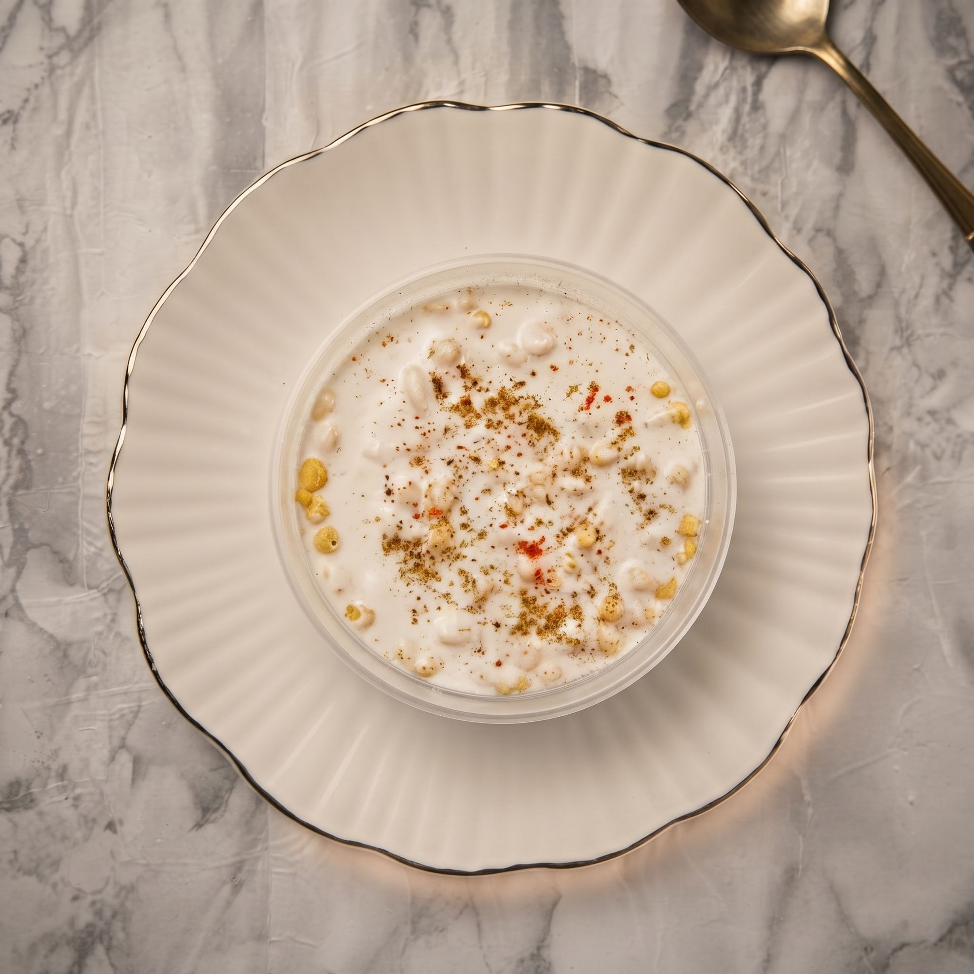 White bowl of creamy oatmeal on a gold-rimmed plate with cinnamon on a marble table