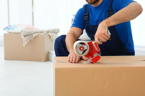 A man is taping a cardboard box with tape.