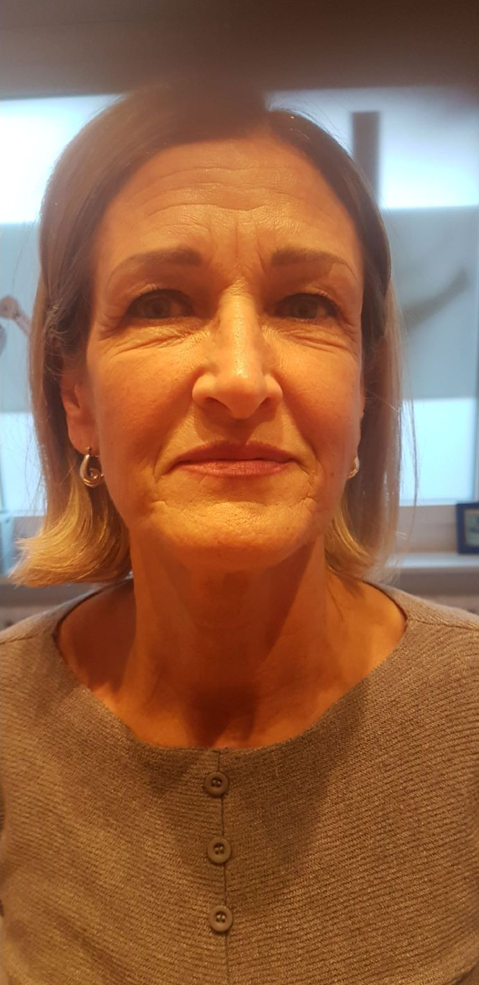 una donna indossa un maglione grigio e orecchini e sorride alla telecamera .