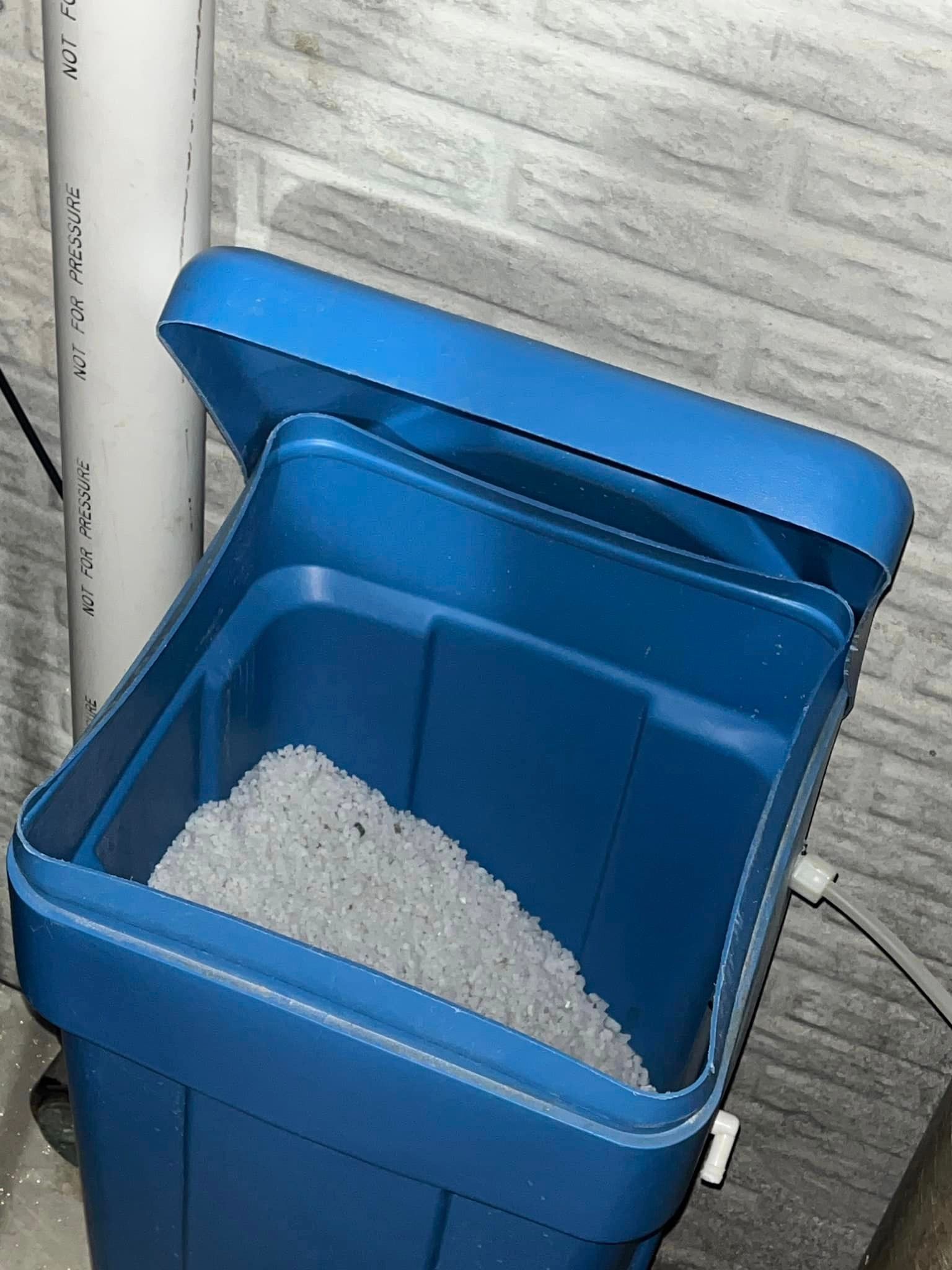 A blue trash can filled with a lot of gray powder.