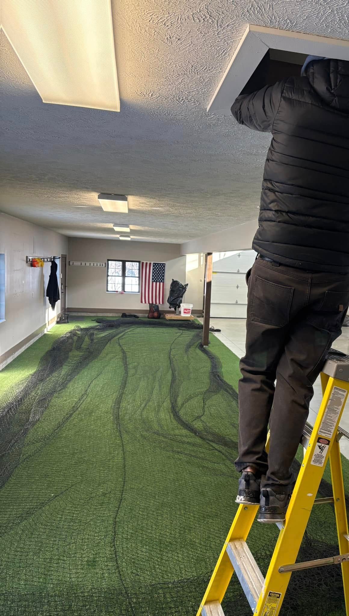 A man is standing on a ladder in a garage working on the ceiling.