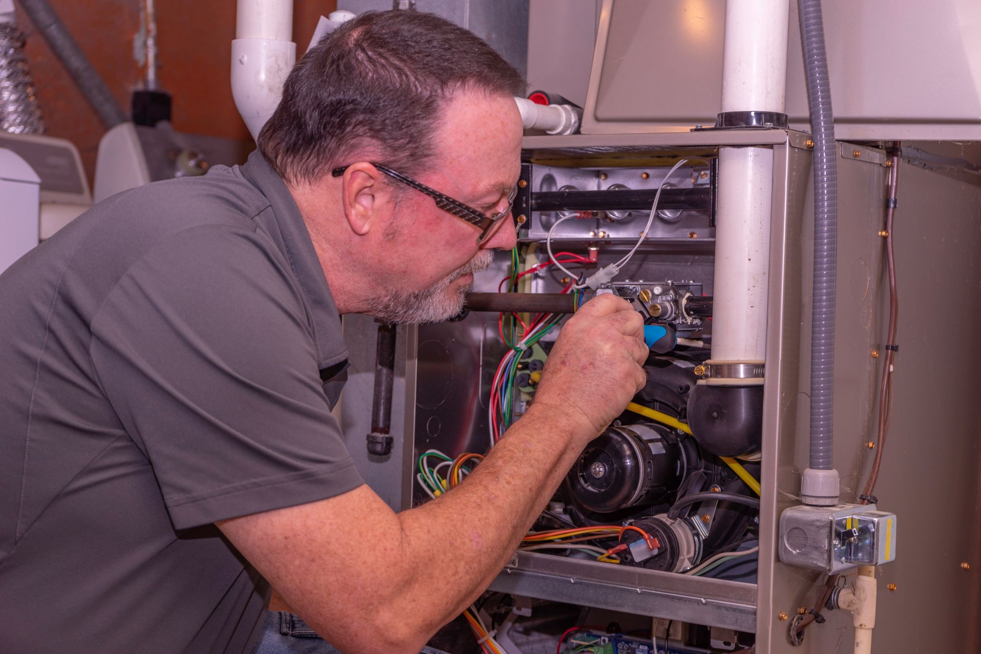 Man in glasses working on furnace, focused, in a mechanical room with wires and pipes. Man in glasses working on furnace, focused, in a mechanical room with wires and pipes.