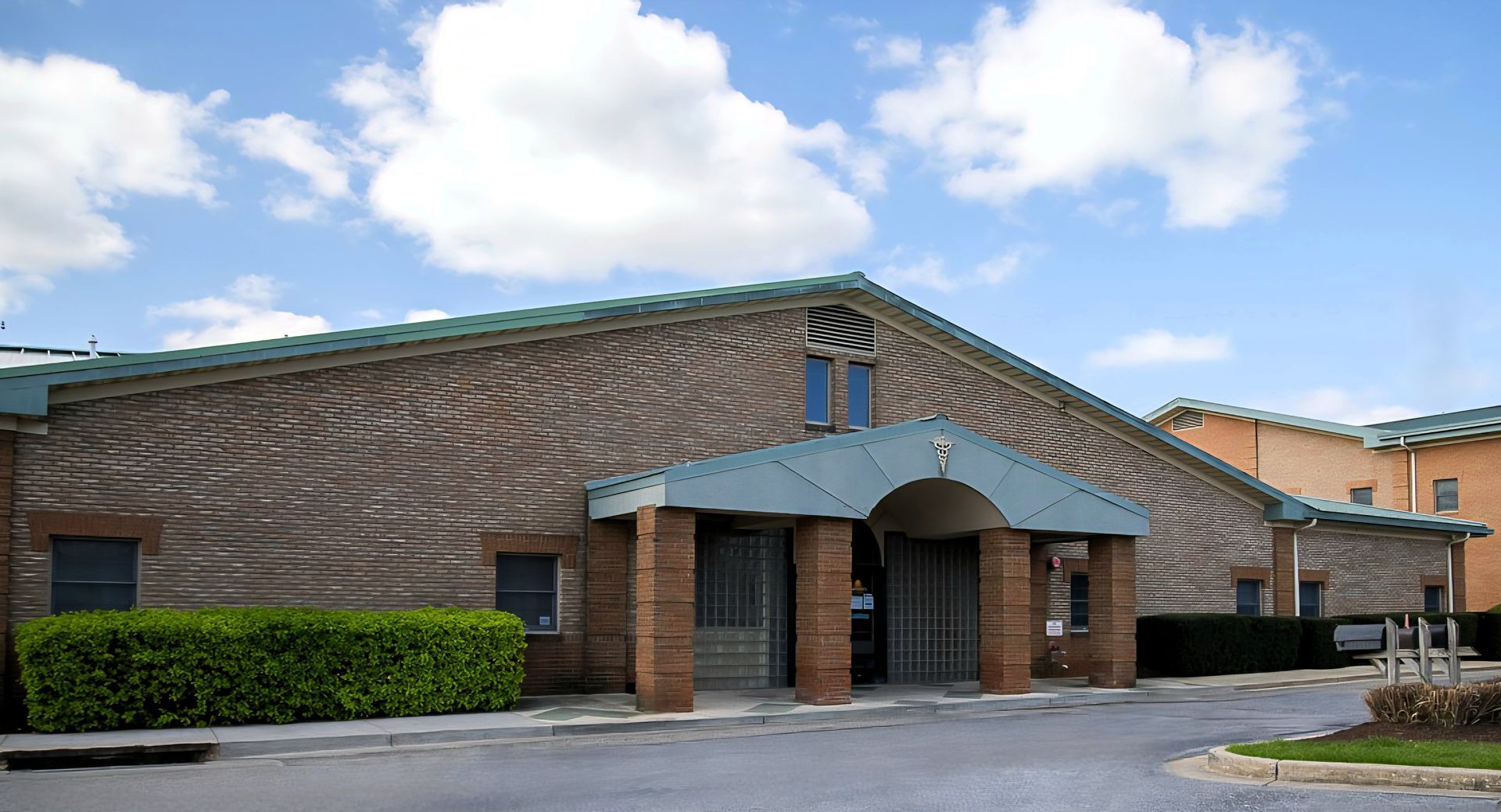 Brick building with arched entrance and blue awning under a partly cloudy sky