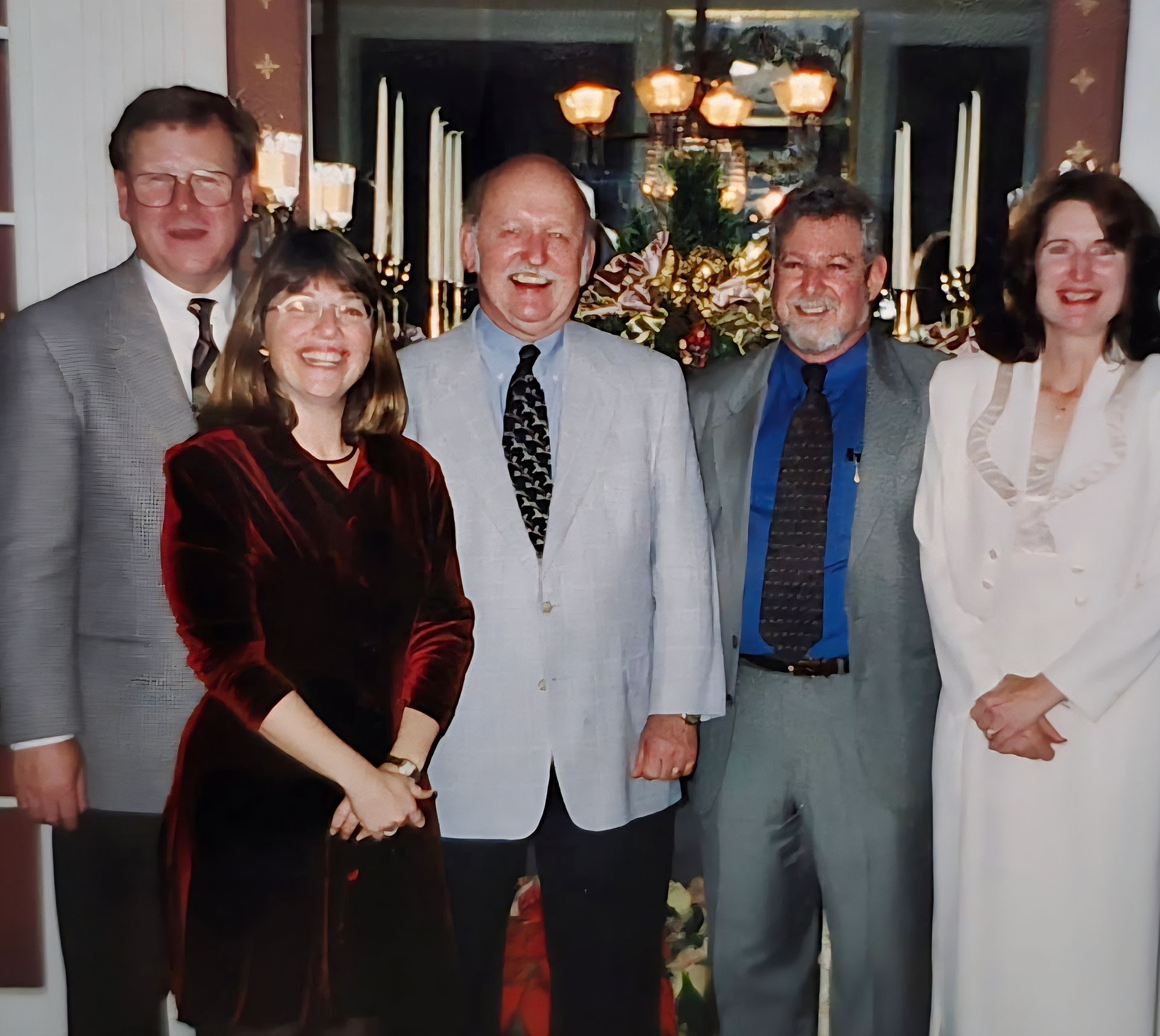 Five people posing indoors at a formal event, dressed in suits and dresses.
