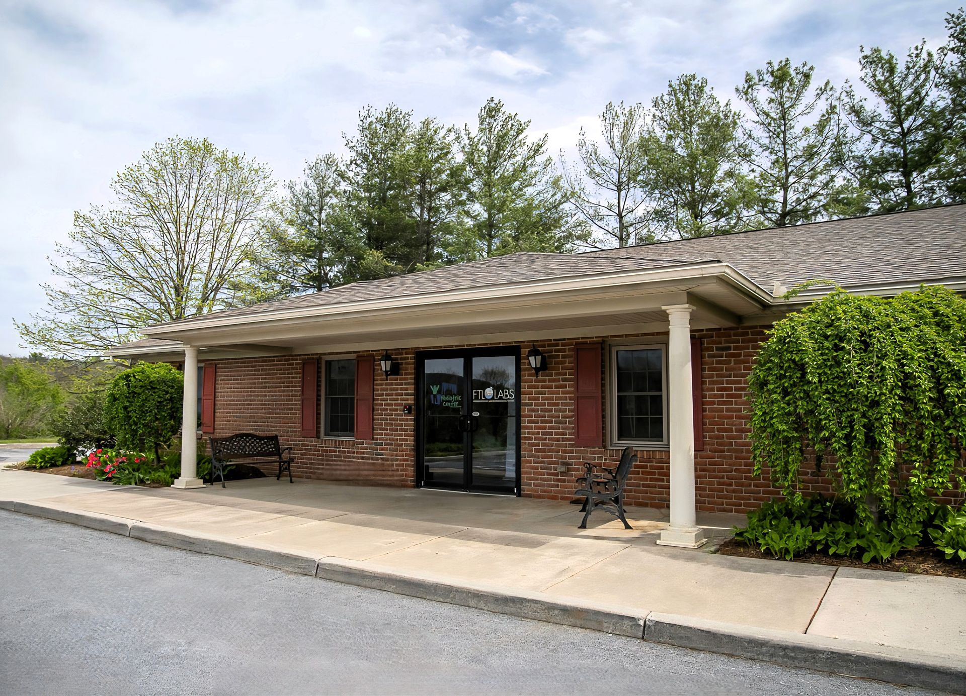 Brick storefront with covered entrance, glass doors, white columns, and a bench outside
