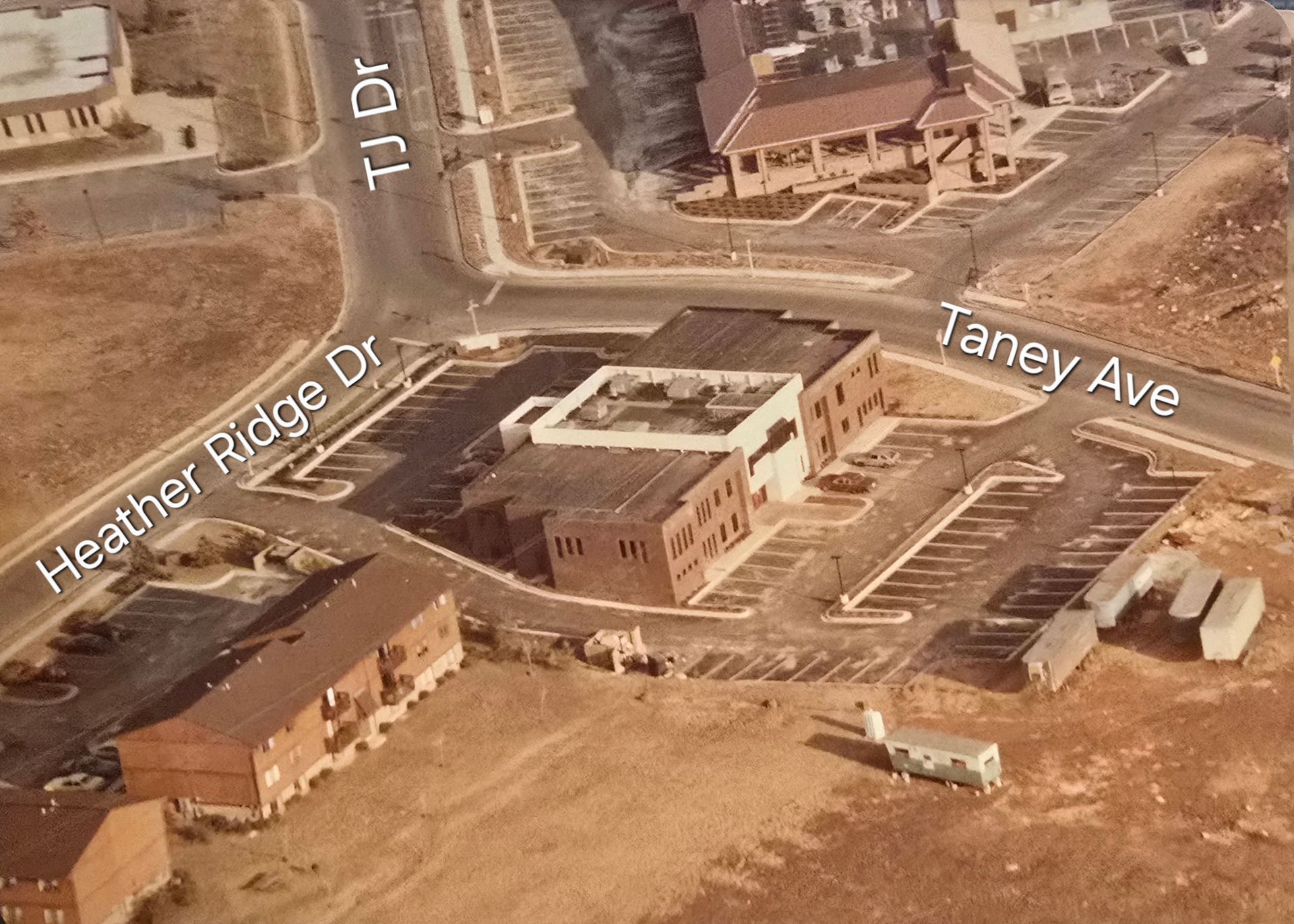 Aerial view of a construction site with brick buildings, roads, and parking lots labeled Heather Ridge Dr and Taney Ave