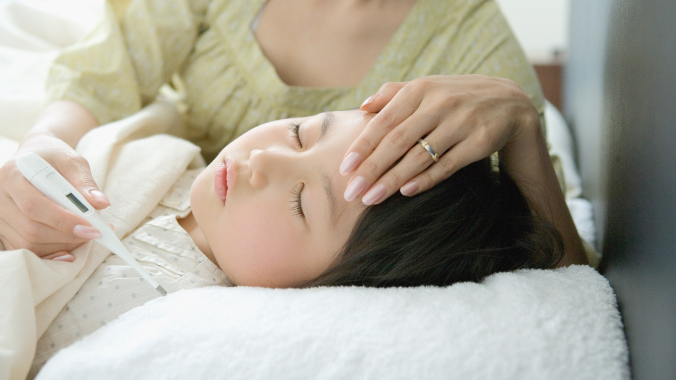 Woman checks a resting person's temperature with a hand on the forehead and a thermometer nearby