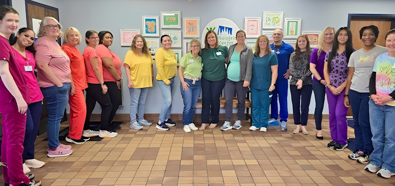 Group of people in colorful shirts standing together in a hallway, smiling for a group photo.