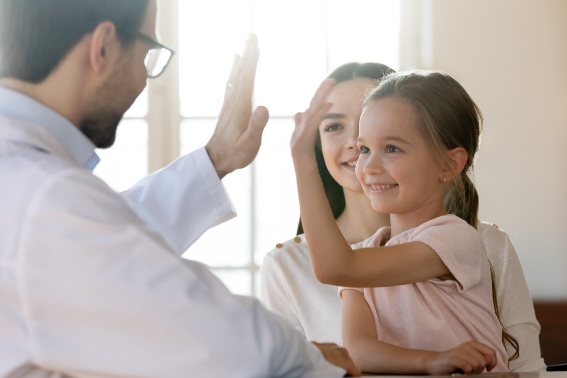 Doctor high-fiving a smiling child in a clinic, with a woman standing behind them