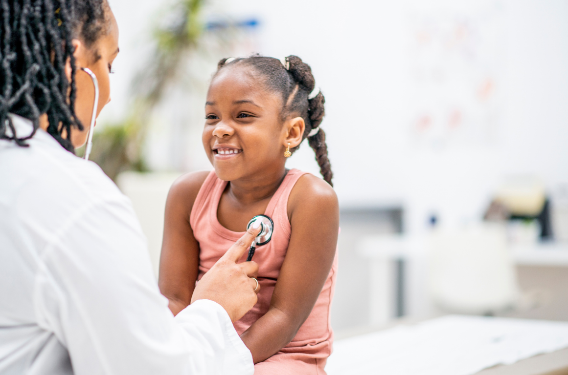 Doctor listening to a smiling child’s chest with a stethoscope in a clinic