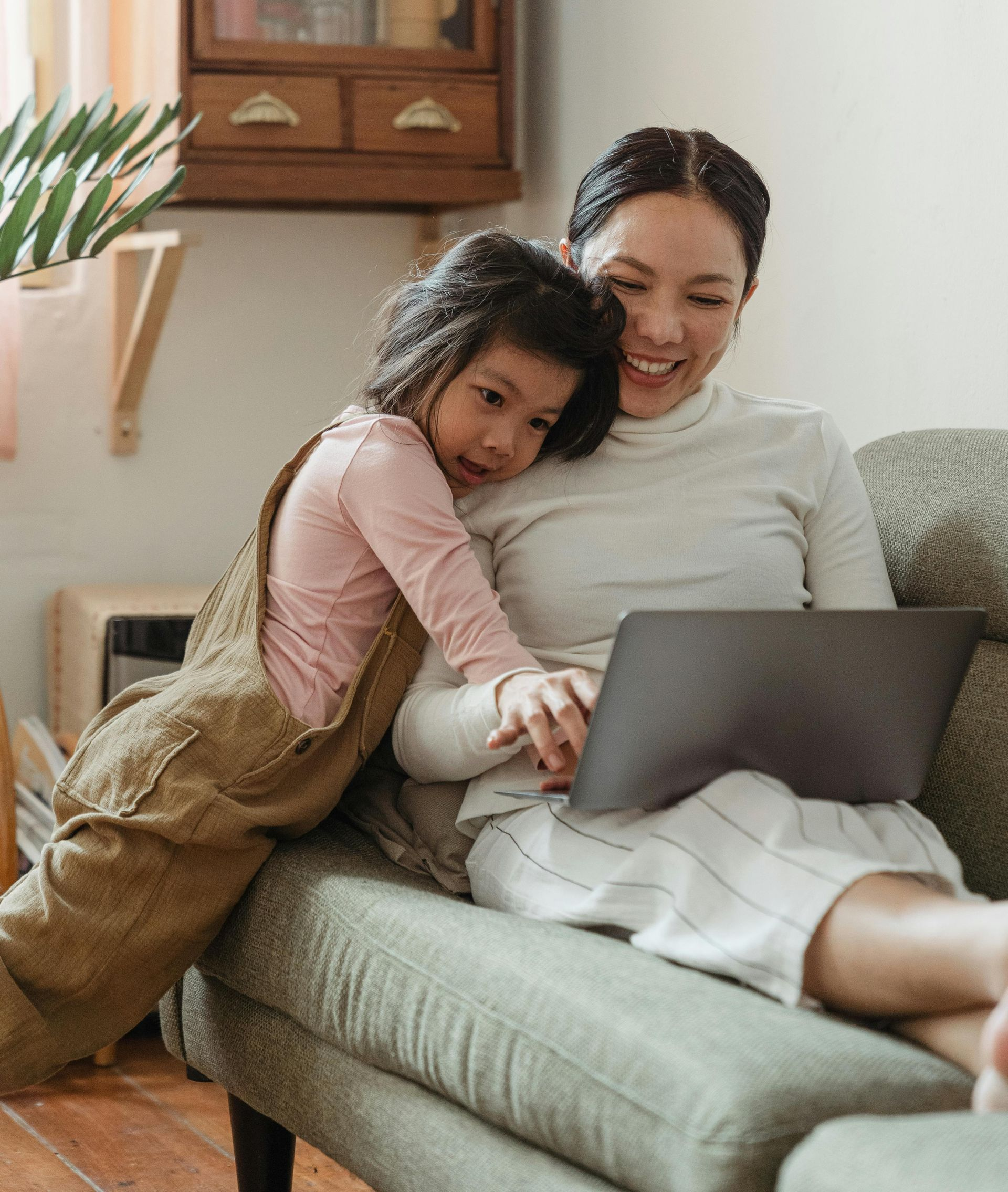 Woman and child cuddling on a couch while looking at a laptop in a cozy living room