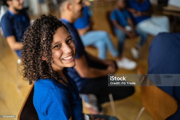 Smiling student in a blue shirt seated in a classroom, looking toward the camera.