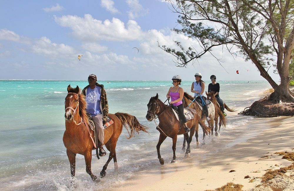 Beach in Cayman Islands near one of our properties to buy or rent. People riding horses on a beach.