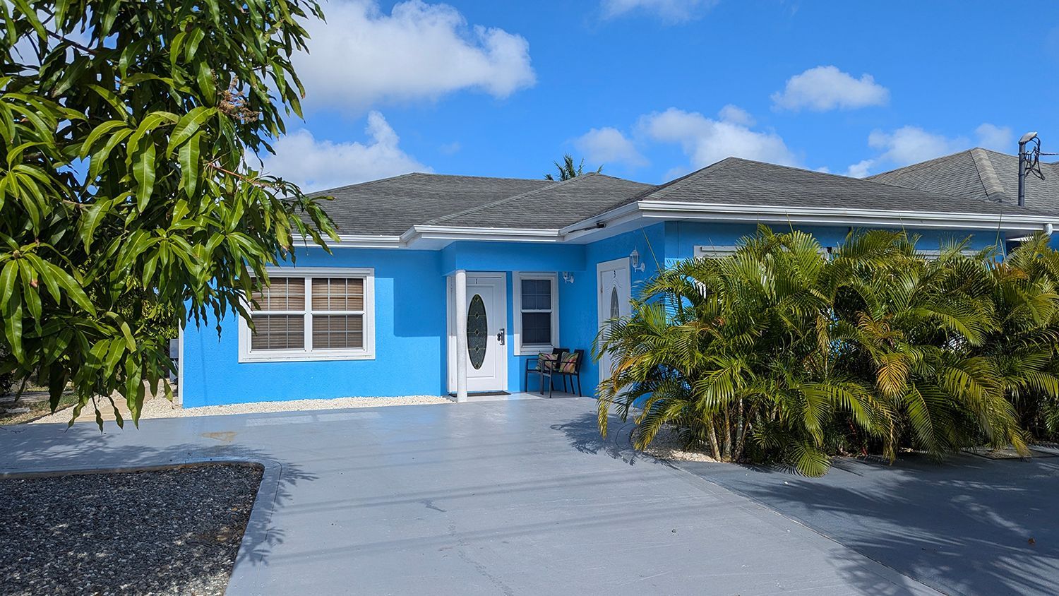 One of our properties to buy or rent in the Cayman Islands. Blue house with grey roof and driveway and clear sky.