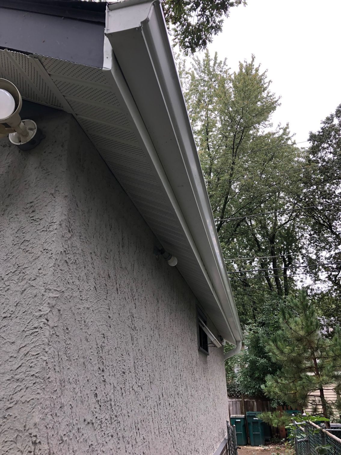 A white gutter on the side of a house with trees in the background.