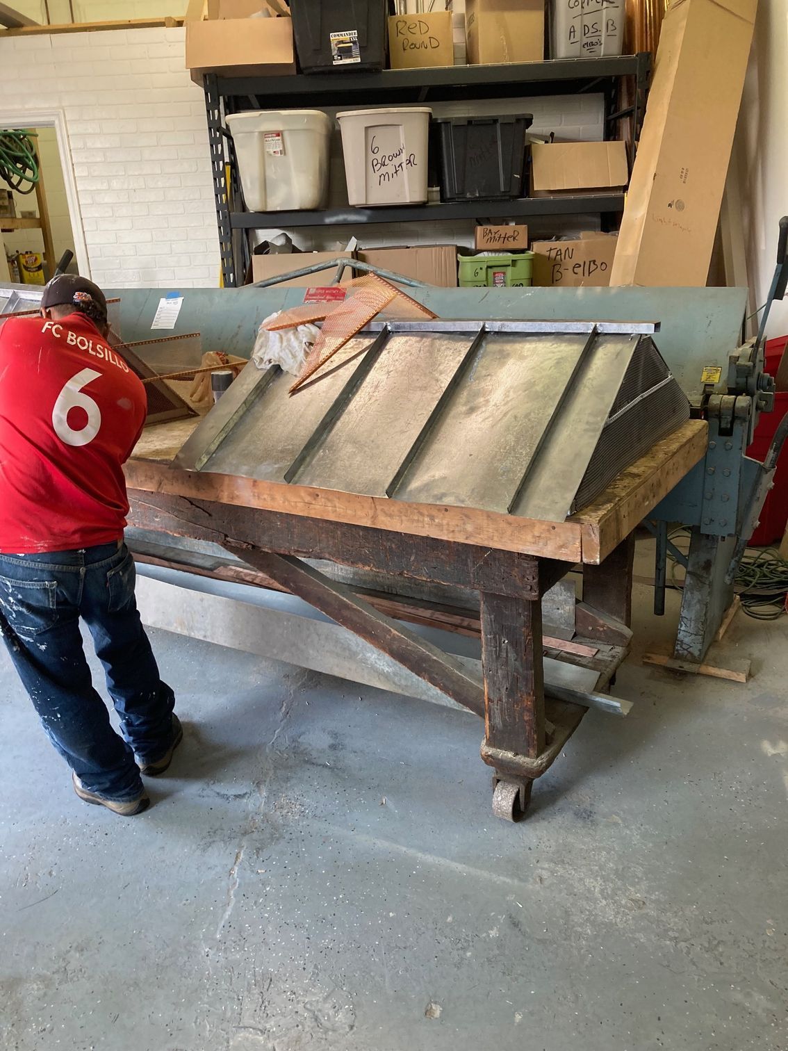 A man wearing a red shirt with the number 6 on it is working on a wooden table.