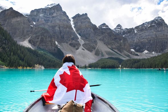 Person in a canoe draped in a Canadian flag on a turquoise lake with mountains in the background.
