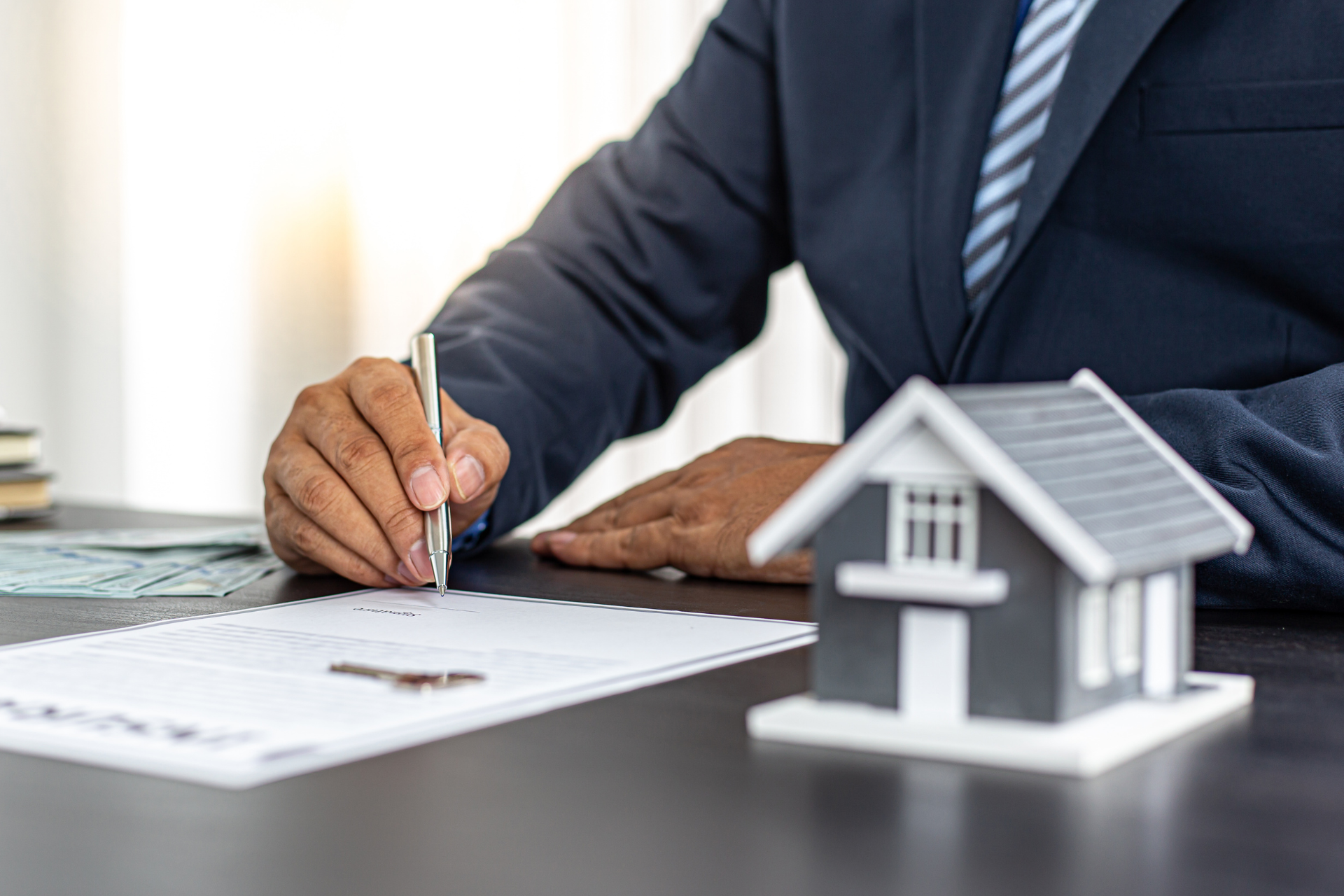 Businessperson signing a document beside a small house model on a desk