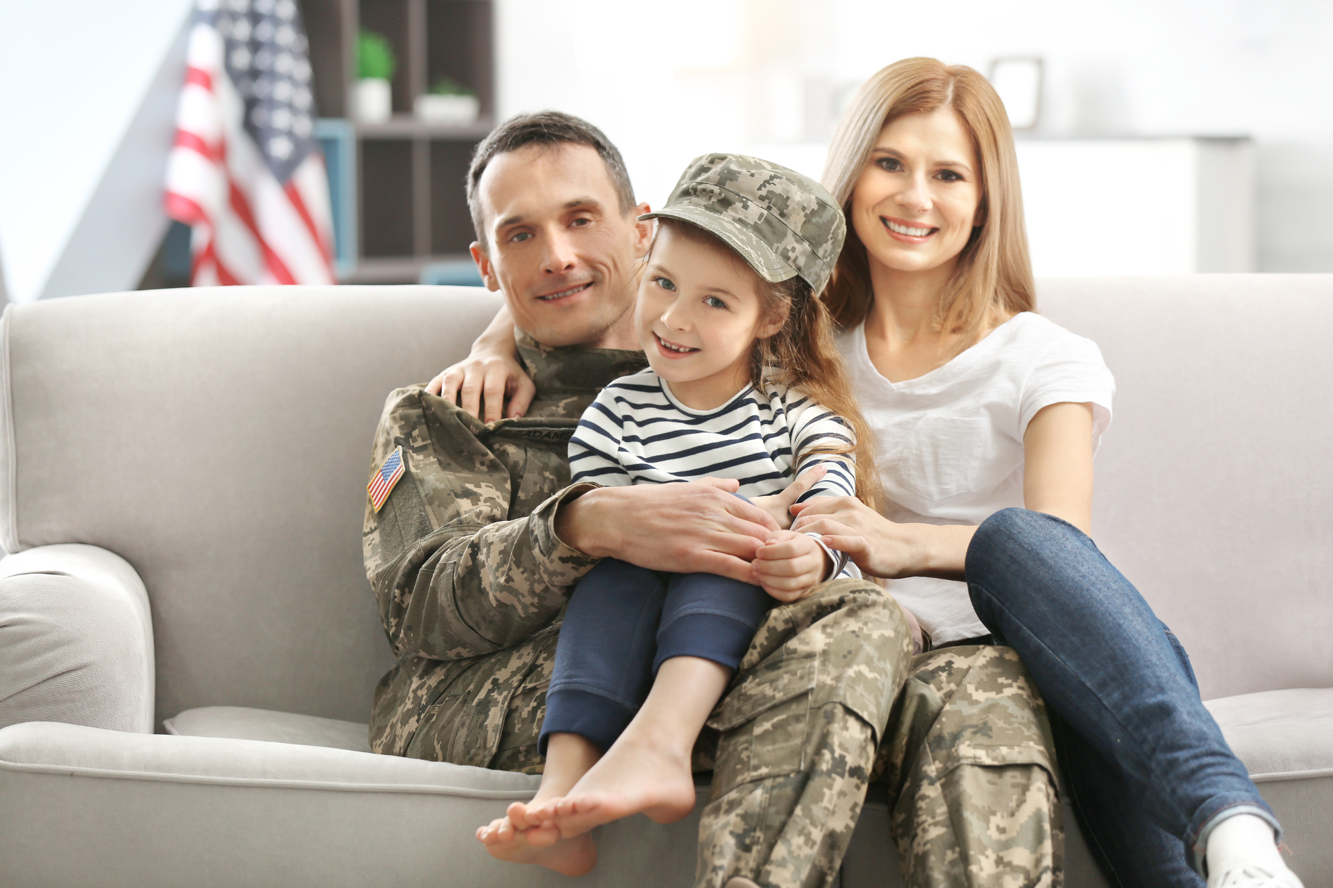 Family of three sitting on a couch, smiling together in a bright living room.