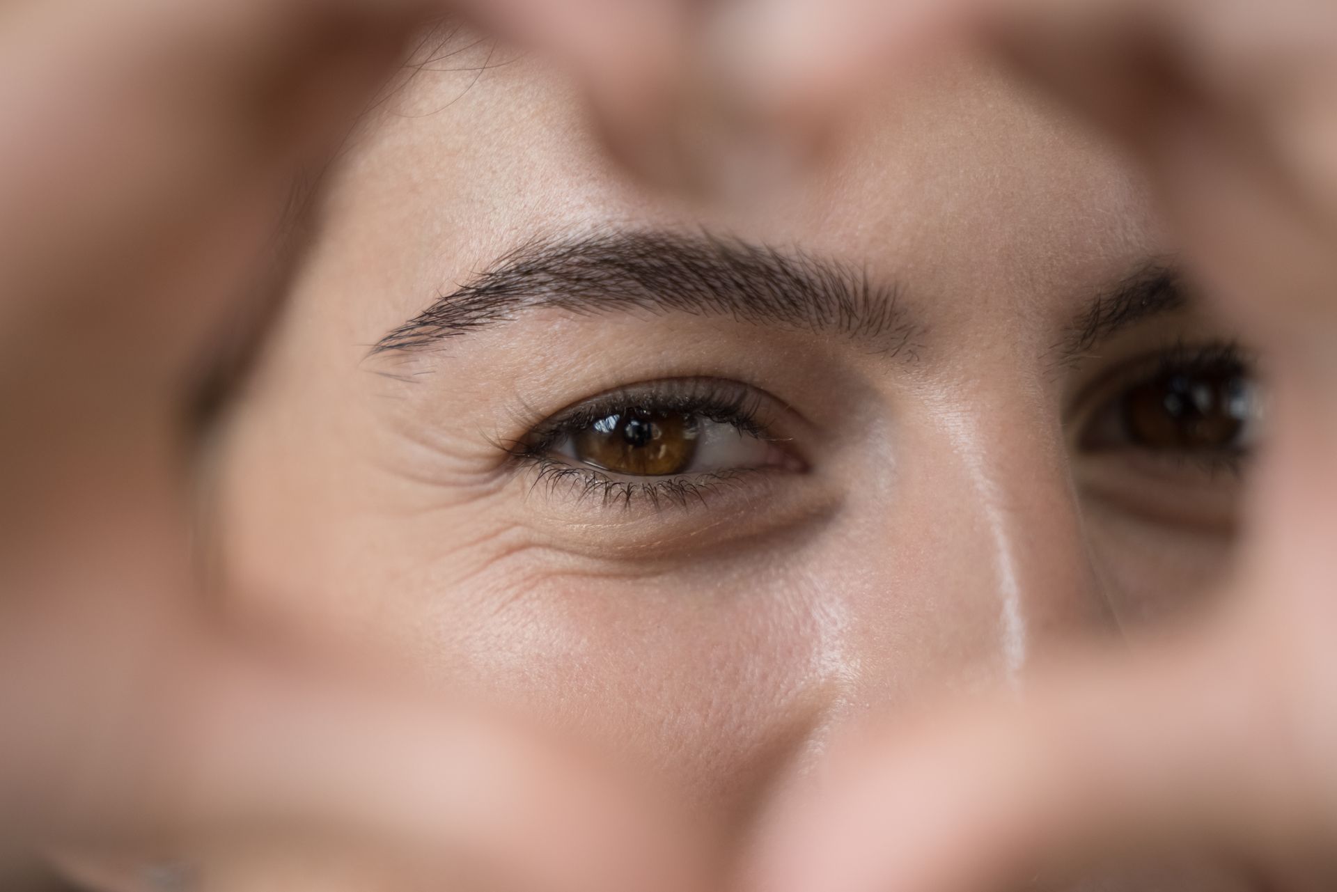 Close-up of a smiling face framed by hands in the foreground