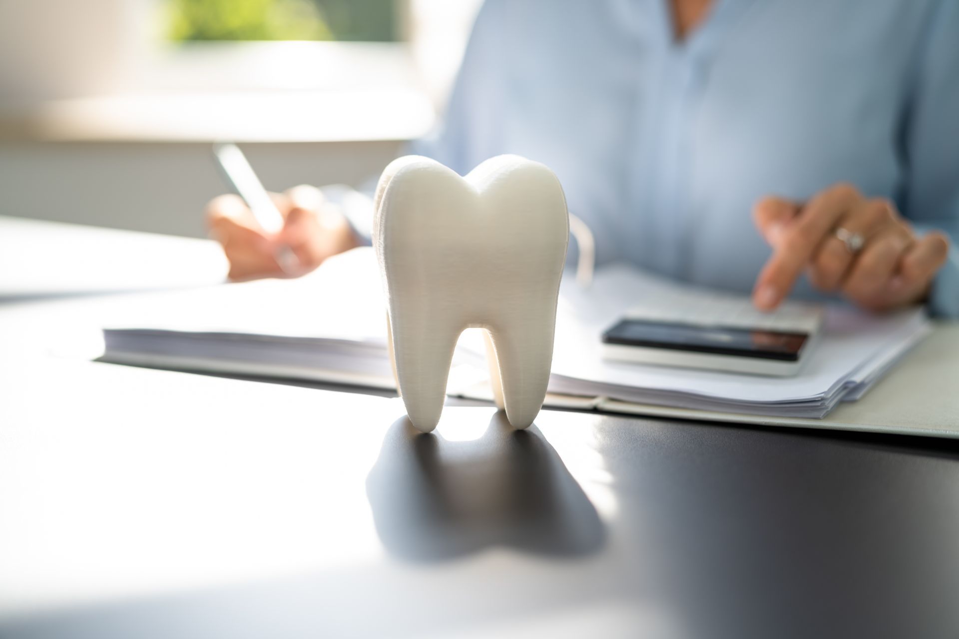 White tooth-shaped figurine on a desk in front of a person writing on paperwork