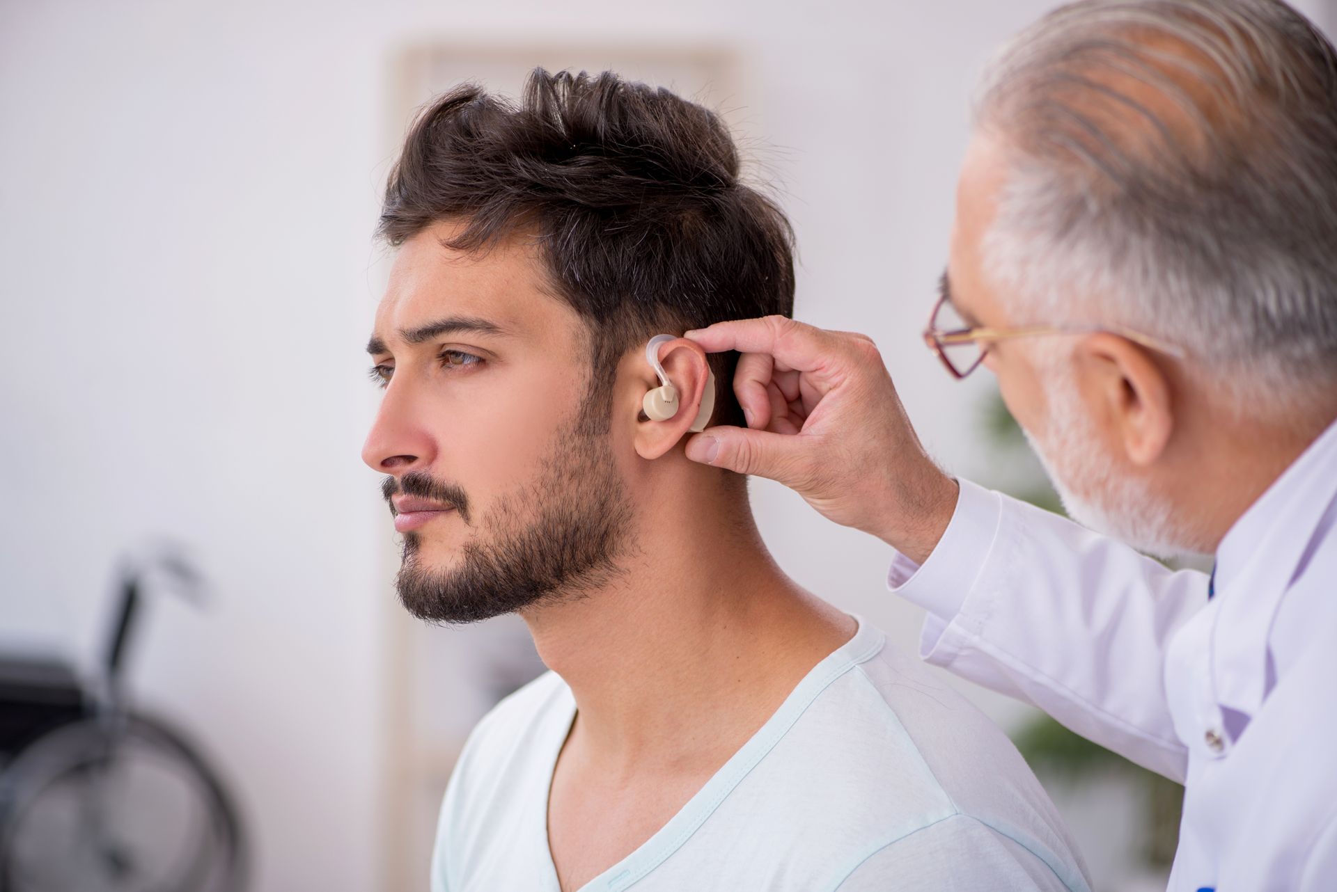 Doctor fitting a hearing aid on a seated man in a clinic