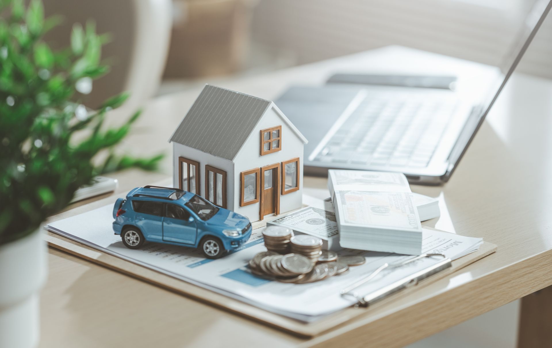Miniature house and blue car on papers beside coins and calculator on a desk