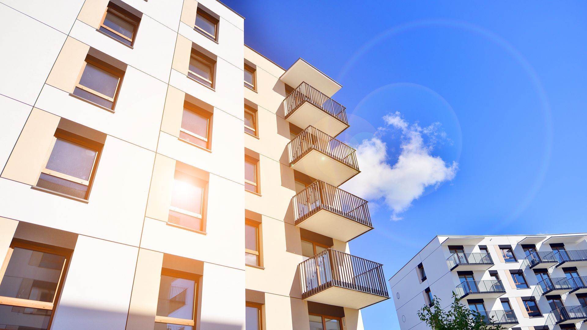 Sunlit apartment buildings with balconies against a bright blue sky and clouds