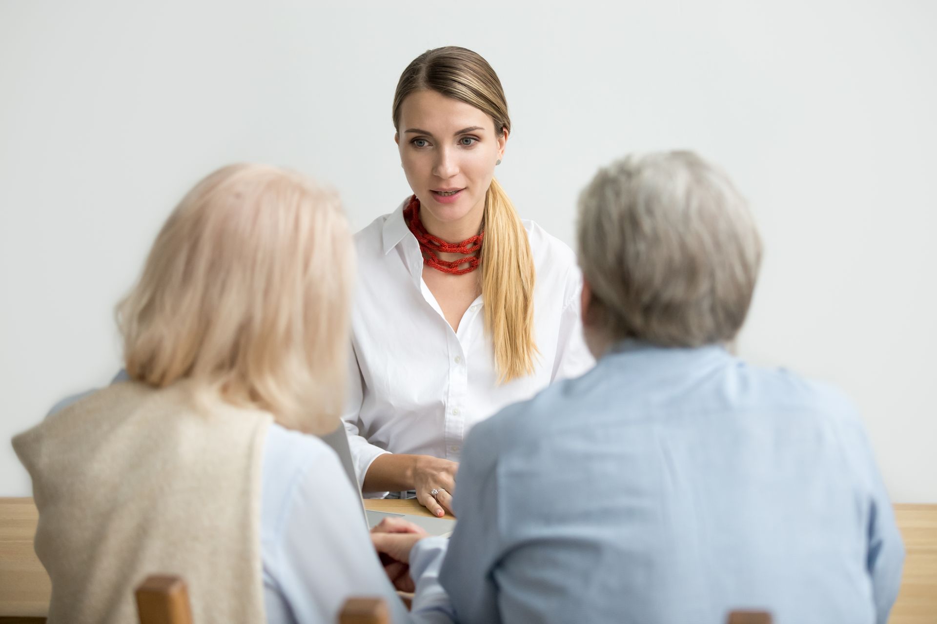 Woman in white coat speaking to two seated people in a bright office meeting