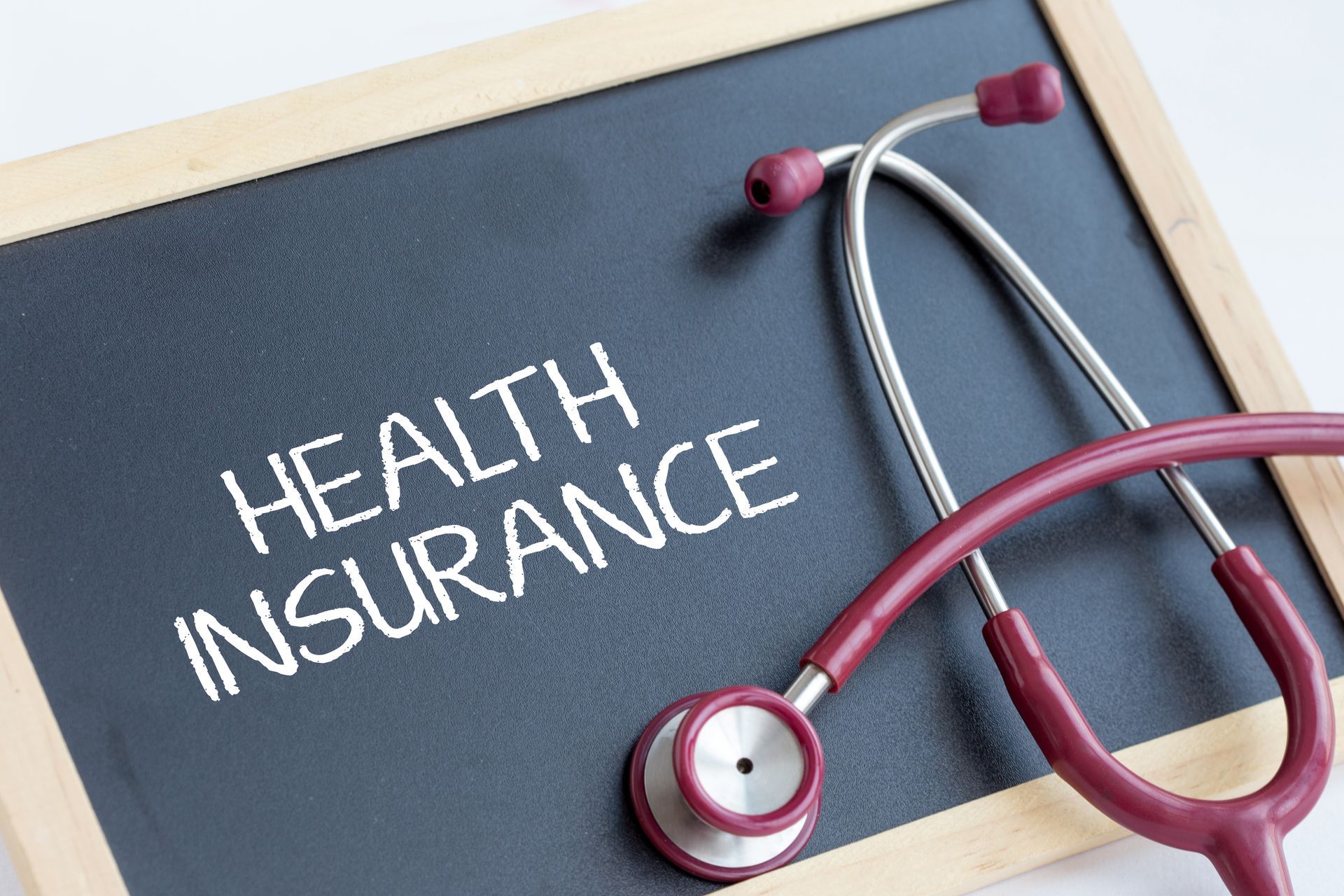 Health insurance written on a chalkboard beside a stethoscope