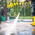Person power-washing a patio with a yellow hose and wand outdoors