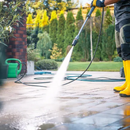 Person power-washing a patio with a yellow hose and wand outdoors