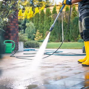 Person power-washing a patio with a yellow hose and wand outdoors
